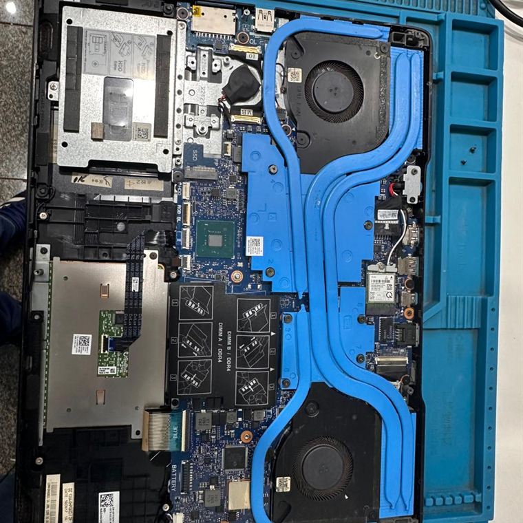 Notebook Dell aberto na bancada sobre tapete antiestático, com a placa-mãe, os dois coolers e os heatpipes à mostra