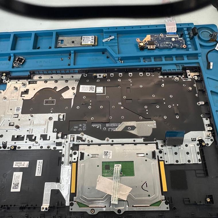 Base de notebook desmontada no tapete de reparo, com SSD M.2, placa de USB e parafusos separados nas divisórias