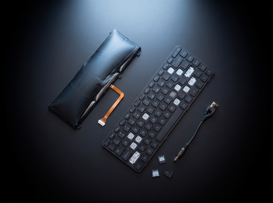 Bateria de notebook estufada, teclado com teclas faltando e conector de carga queimado sobre a bancada